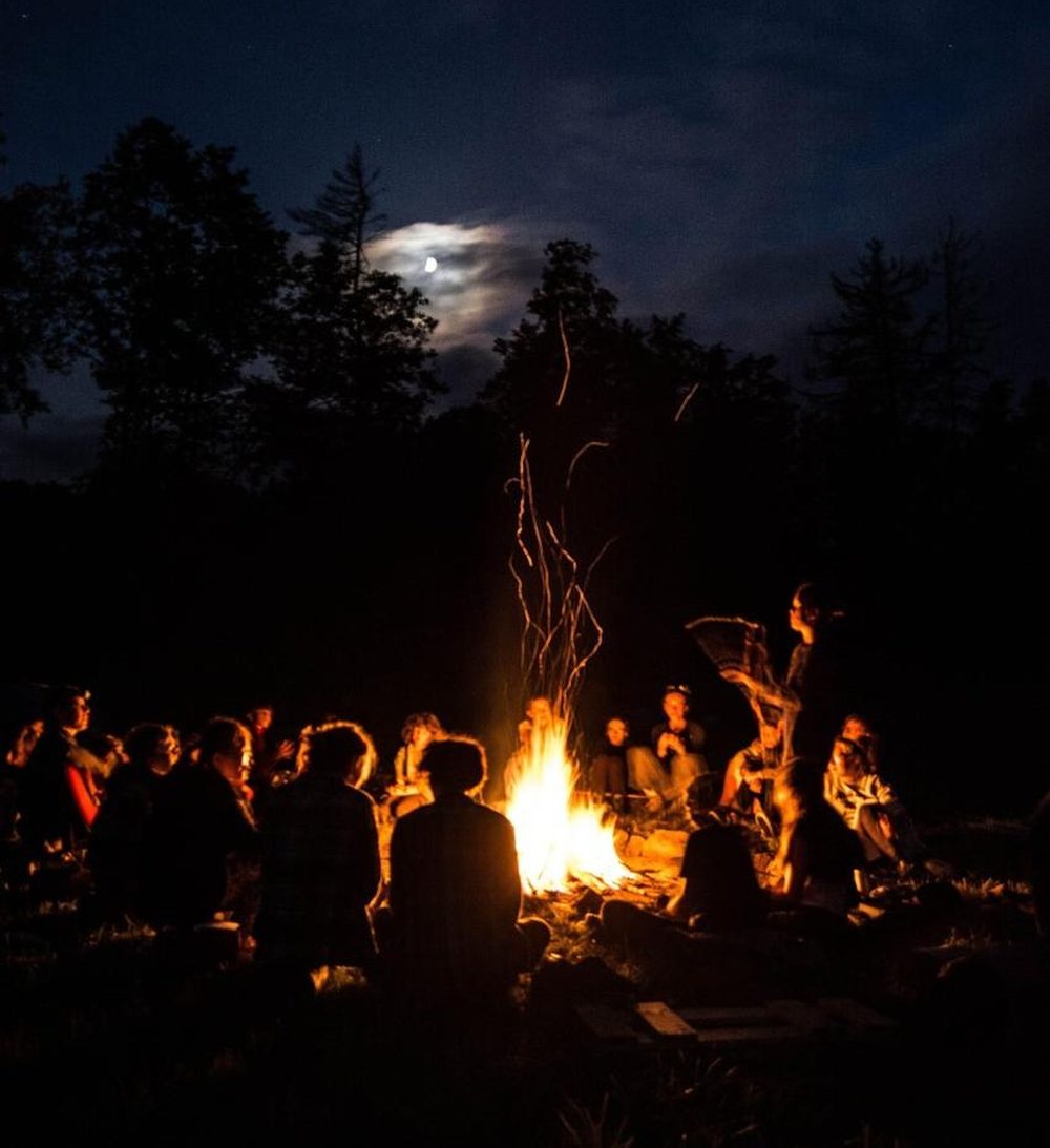 Guests gathered around a campfire under a moonlit sky